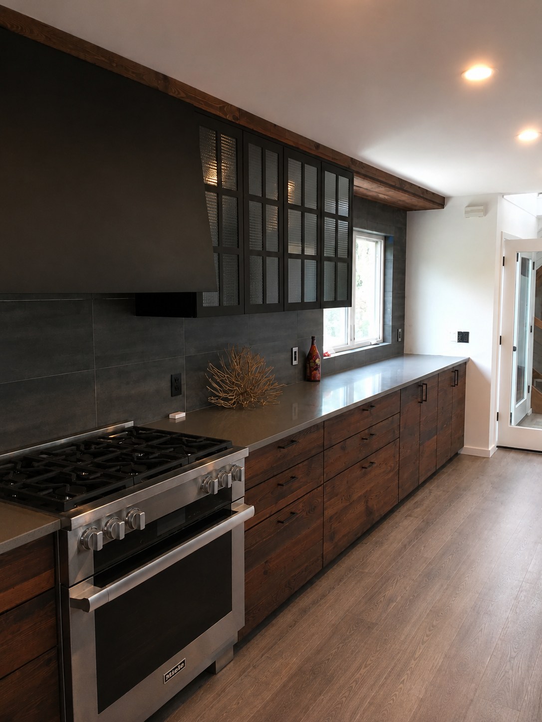 Long view of a modern kitchen renovation with reclaimed wood cabinetry, Miele professional range, gray stone tile backsplash, and exposed ceiling beam — New York City by FF Solutions